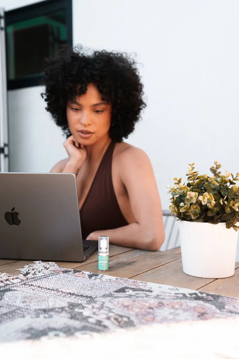 A woman working at a laptop with a Focus spray on the table